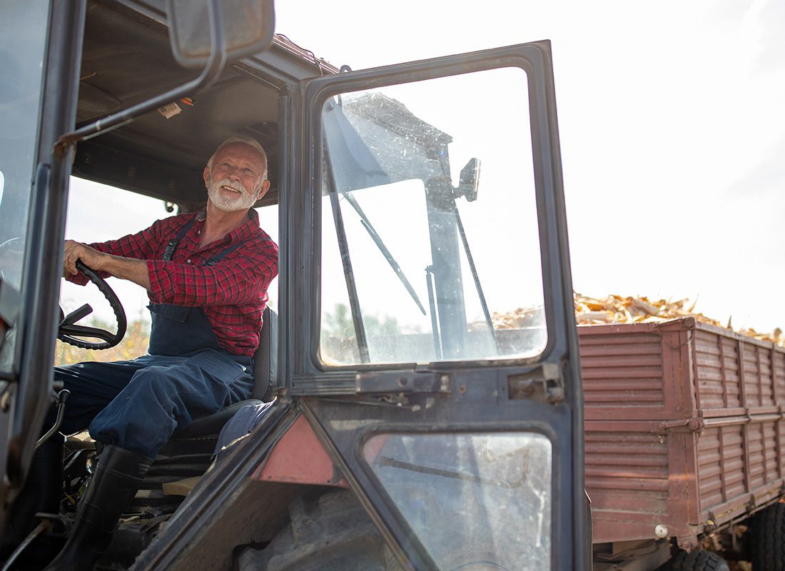 Business Insurance - Portrait of an Elderly Farmer Driving a Tractor on His Farm on a Sunny Fall Day with a Trailer Full of Corn