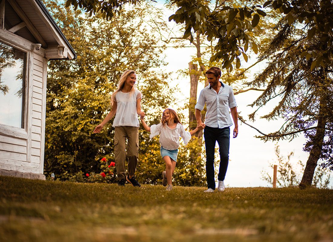 Insurance Solutions - View of a Mother and Father Holding Hands with Their Daughter as They Walk in Their Backyard on a Sunny Day