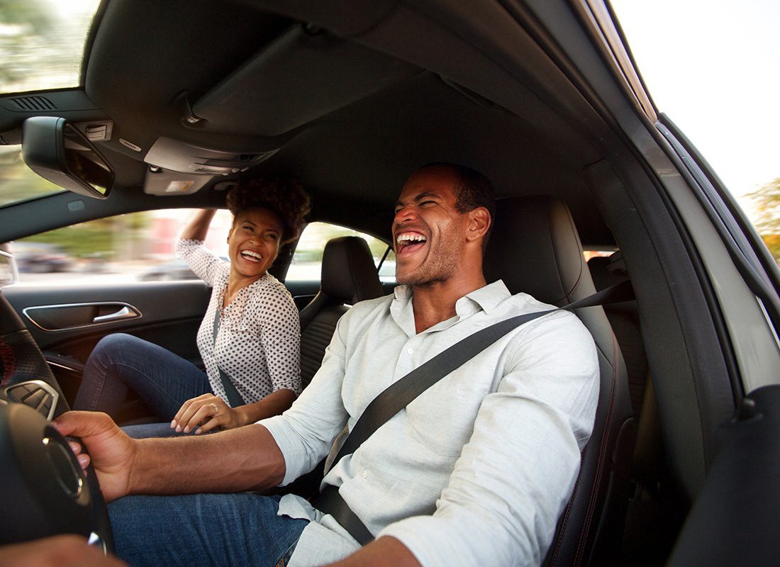 Personal Insurance - Closeup Portrait of a Young Couple Sitting and Laughing While Sitting in a Car During a Road Trip